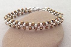 a silver and gold beaded bracelet sitting on top of a rock