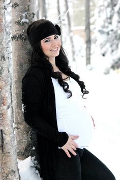 a pregnant woman leaning against a tree in the snow