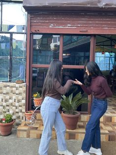 two young women are standing in front of a store window and pointing at each other