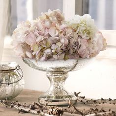 a glass bowl filled with lots of flowers on top of a wooden table next to a window