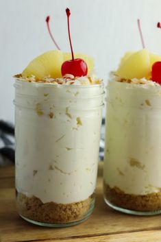 two desserts with pineapple slices and cherries on top sit in glass jars