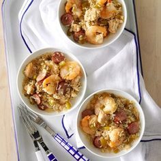 three bowls filled with shrimp and rice on top of a white tray next to silverware