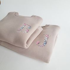 two pink sweaters with embroidered letters on them