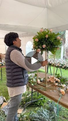 a woman is arranging flowers on a table in front of a white tent with tables and chairs