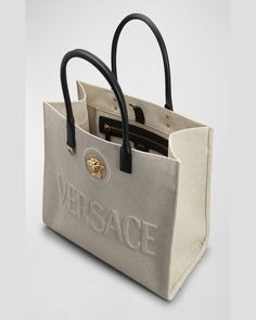 Versace canvas and acrylic tote bag with embossed logo and Medusa head accent     Rolled top handles     Open top with snap strap closure     Interior, one zip pocket    Approx. 11.4"H x 15"W x 7.4"D    "La Medusa" is made in Italy Designer Canvas Bag With Top Handle, Designer Canvas Bag With Top Handle For Errands, Beige Double Handle Bag With Logo, Designer Canvas Shoulder Bag With Handles, Designer Canvas Tote Bag With Top Handle, Designer Canvas Tote Bag With Top Carry Handle, Designer Canvas Bag With Top Carry Handle For Errands, Designer Canvas Bag With Double Handle For Errands, Designer Canvas Bag With Double Handle For Daily Use