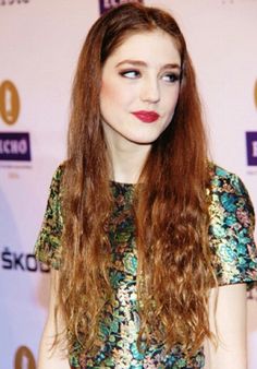 a woman with long red hair standing in front of a wall