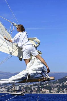 a man in white is standing on the side of a sailboat while looking out over the water