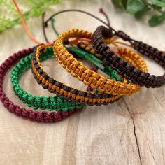 four braided bracelets sitting on top of a wooden table next to green leaves