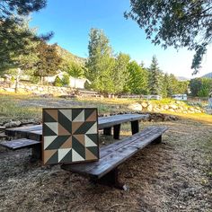 a wooden bench sitting in the middle of a field with a patchwork quilt on it