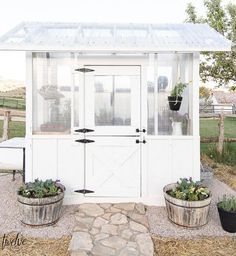 a small white shed with two planters on the front and one in the back