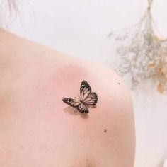 a small butterfly tattoo on the back of a woman's left shoulder, it is black and white