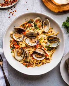 a plate of pasta with clams and parmesan cheese on the side next to silverware