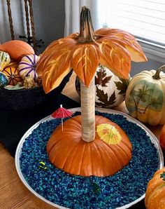 pumpkins and gourds are sitting on a table with blue gravel in the center