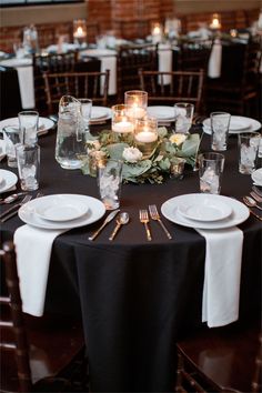 the table is set with black linens and white place settings, candles in glass vases