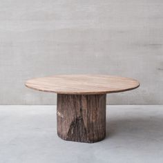 a round wooden table sitting on top of a cement floor next to a white wall