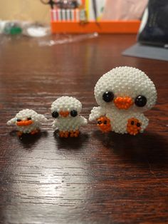 three little white birds sitting on top of a wooden table next to an orange and black bird