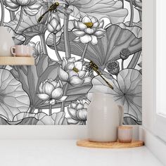 a white vase sitting on top of a counter next to a wall mounted mural with flowers