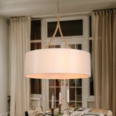 a chandelier hanging over a dining room table with white linens on it