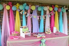 a table topped with lots of colorful balloons and desserts next to a brick wall