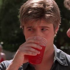 a young man drinking from a plastic cup while standing next to other people in the background