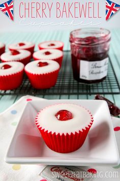 red velvet cupcakes with white frosting and cherries on a plate next to jam