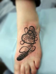 a small tattoo on the foot of a person with a feather and dream catcher in it