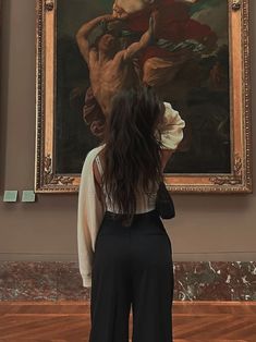 a woman standing in front of a painting with her back to the camera and looking at it