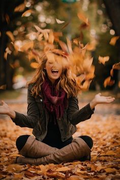 a woman is sitting on the ground with her hands in the air and falling leaves