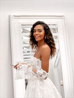 a woman standing in front of a mirror wearing a white wedding dress with long sleeves