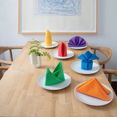 colorful paper napkins on white plates sit on a wooden table in front of a framed drawing