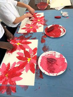 children are painting flowers on paper plates at a table with other kids's artwork