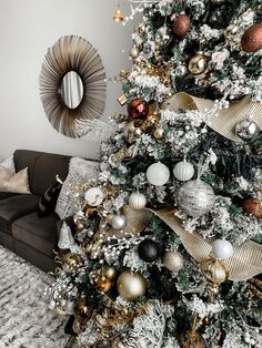 a christmas tree with gold, silver and white ornaments on it in a living room