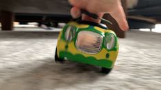 a small toy car is being held by someone's hand on the floor in front of a vehicle