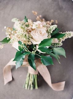 a bridal bouquet with white flowers and greenery on the bottom, tied in brown ribbon