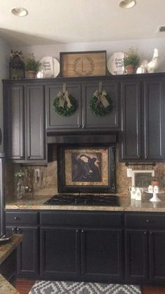 a kitchen with black cabinets and christmas wreaths on the wall above the stove top