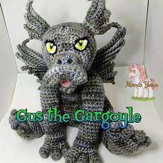 a crocheted gray dragon sitting on top of a white chair with yellow eyes