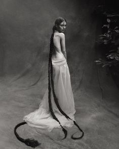 a woman with long braids standing in front of a black and white background wearing a dress