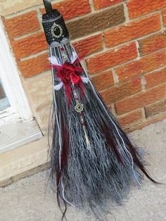 a broom that has been decorated with feathers and red ribbon on the side of a brick building