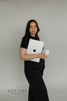 a woman in black holding a white apple laptop and a coffee cup with her hands