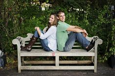 a man and woman sitting on a bench in front of some trees with their arms around each other