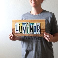 a woman holding up a wooden sign with the word luvumor written on it