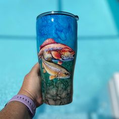 a person holding up a blue cup with fish on it next to a swimming pool