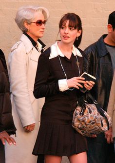 a woman in a short black dress is holding a purse and looking at her cell phone