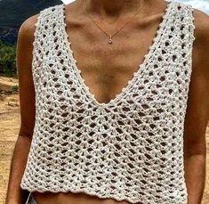 a woman wearing a white crocheted tank top and denim shorts with her hands in her pockets