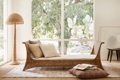 a wicker day bed sitting in front of a large window next to a lamp