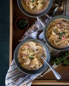 three bowls of soup on a tray with spoons and garnishes in them