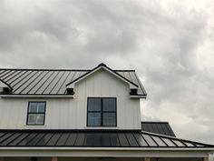 a white house with a metal roof and black shutters on the front door is seen against a cloudy sky