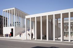 several people are walking around in front of a building with columns on both sides and stairs leading up to the second floor