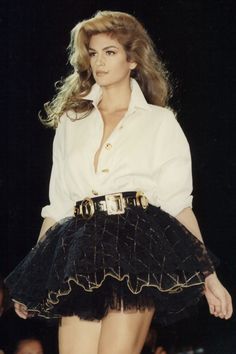 a woman is walking down the runway wearing a black skirt and white shirt with gold buttons