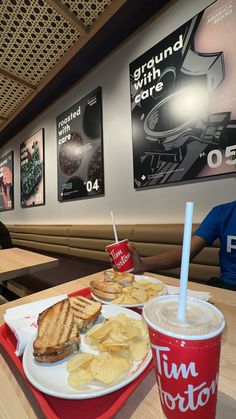 there is a sandwich and chips on the table at this fast food restaurant with two people sitting in the background